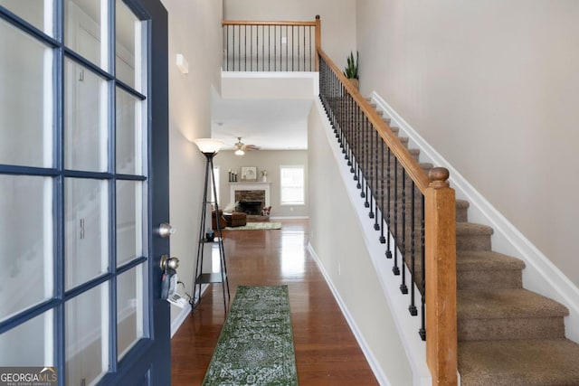 foyer featuring baseboards, a towering ceiling, dark wood-style floors, stairs, and a fireplace