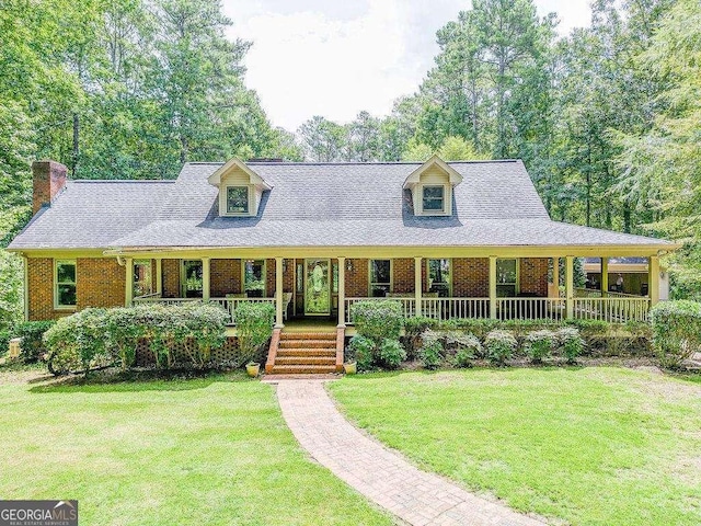 view of front facade with a porch, roof with shingles, a front yard, and brick siding