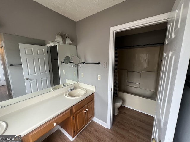 full bath with toilet, vanity, a textured ceiling, wood finished floors, and baseboards