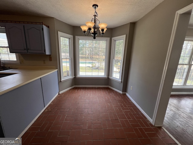 unfurnished dining area with brick floor, plenty of natural light, an inviting chandelier, and baseboards