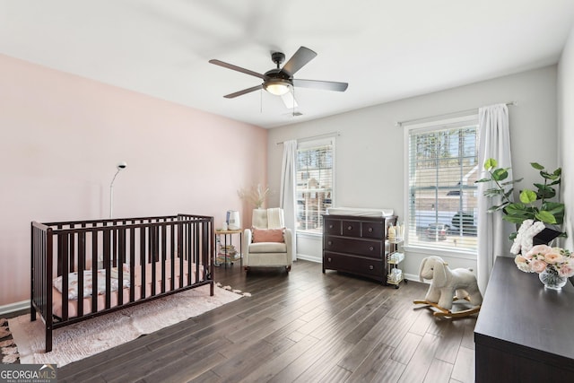 bedroom with visible vents, a crib, ceiling fan, baseboards, and wood finished floors