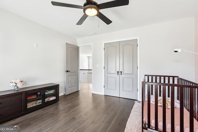 bedroom with a ceiling fan, baseboards, dark wood-style flooring, a nursery area, and a closet