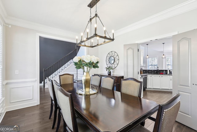 dining area featuring a chandelier, a wainscoted wall, stairs, ornamental molding, and dark wood-style flooring