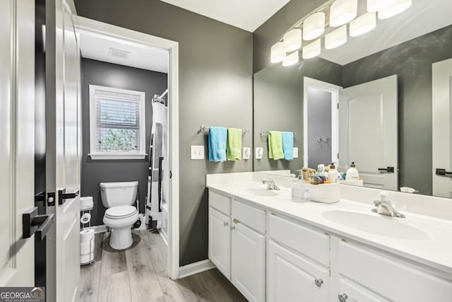 full bath with double vanity, toilet, wood finished floors, and a sink