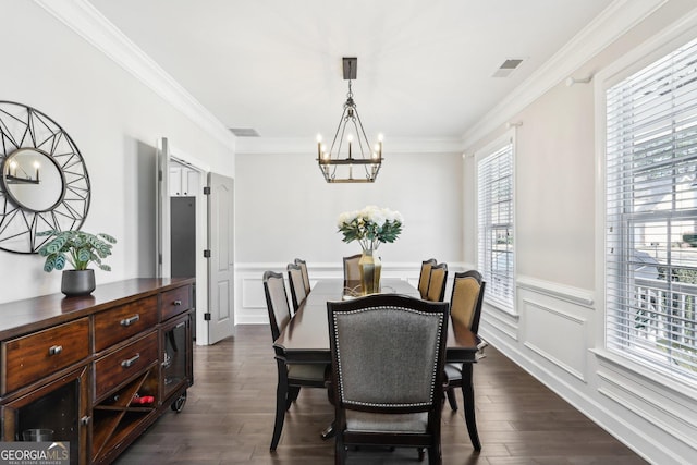 dining room with visible vents, dark wood-type flooring, an inviting chandelier, crown molding, and a decorative wall