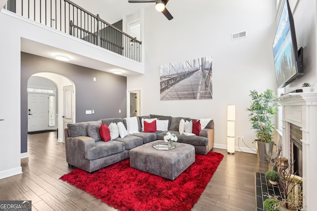 living area featuring wood finished floors, baseboards, visible vents, a fireplace with flush hearth, and arched walkways