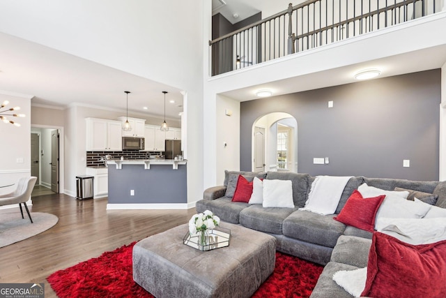 living room featuring baseboards, ornamental molding, a towering ceiling, wood finished floors, and arched walkways