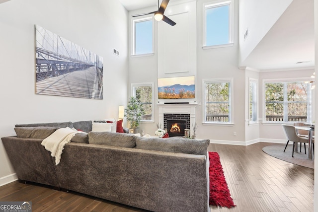 living room with baseboards, visible vents, a fireplace, dark wood-style flooring, and ceiling fan