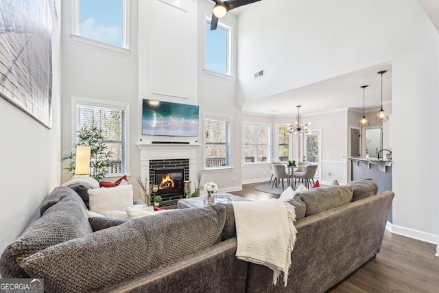 living area with visible vents, dark wood-type flooring, baseboards, a brick fireplace, and a chandelier