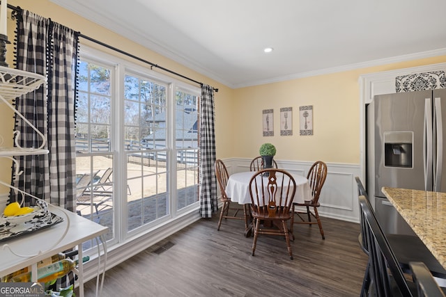 dining area with a decorative wall, a wainscoted wall, dark wood-style flooring, visible vents, and ornamental molding