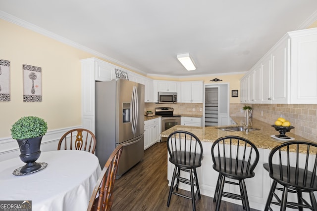 kitchen with dark wood finished floors, stainless steel appliances, white cabinetry, a sink, and a peninsula