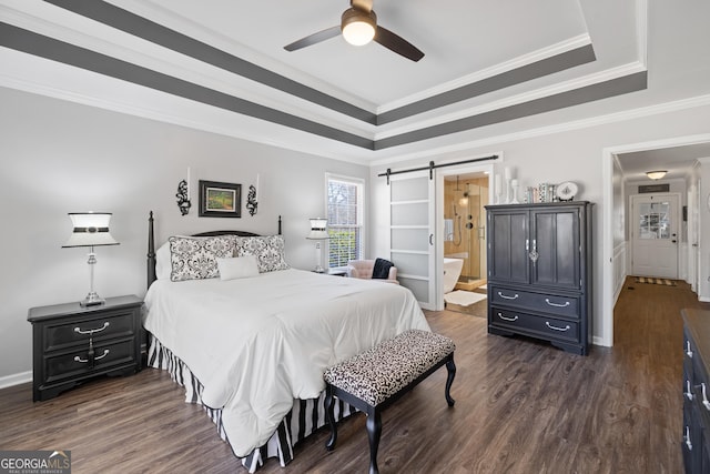 bedroom with dark wood-style flooring, a raised ceiling, ensuite bathroom, ornamental molding, and a barn door