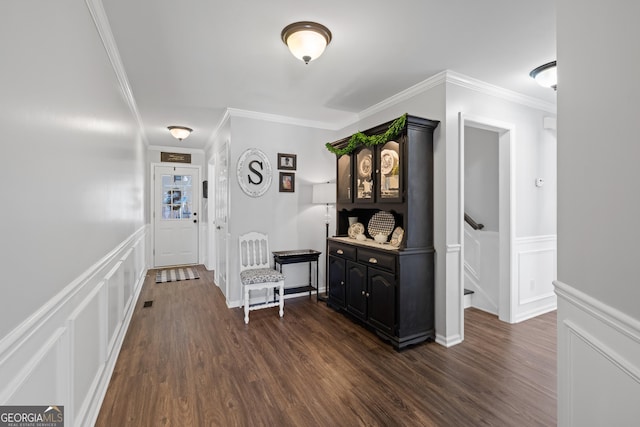 corridor featuring a wainscoted wall, ornamental molding, dark wood finished floors, and a decorative wall