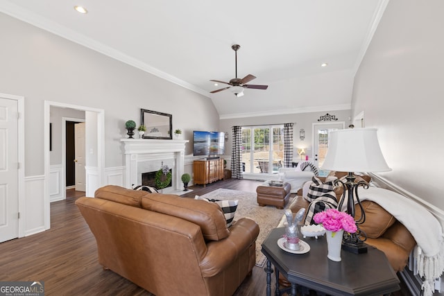 living room featuring a wainscoted wall, lofted ceiling, a fireplace with flush hearth, ornamental molding, and wood finished floors