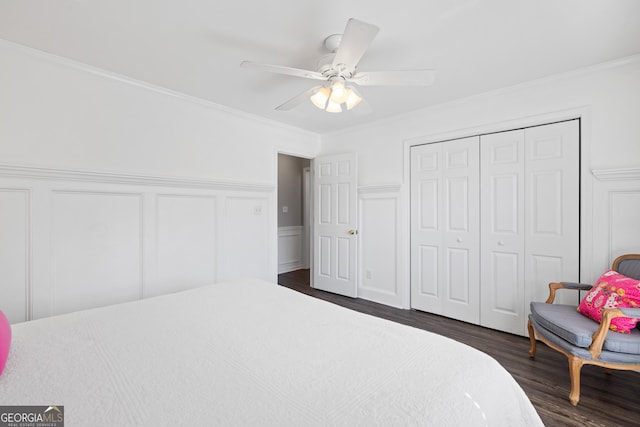 bedroom featuring ceiling fan, a decorative wall, a closet, dark wood-style floors, and crown molding