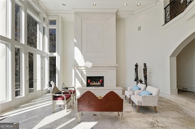 sitting room with a large fireplace, arched walkways, a towering ceiling, crown molding, and recessed lighting