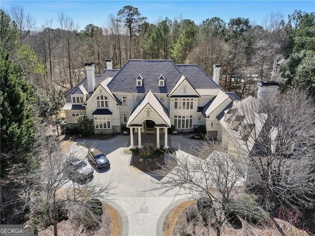 french country home featuring driveway, a chimney, and a wooded view