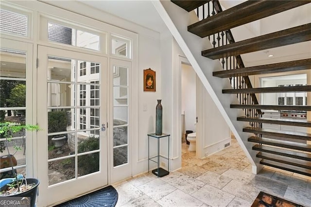 doorway to outside featuring baseboards, stairway, and stone tile flooring