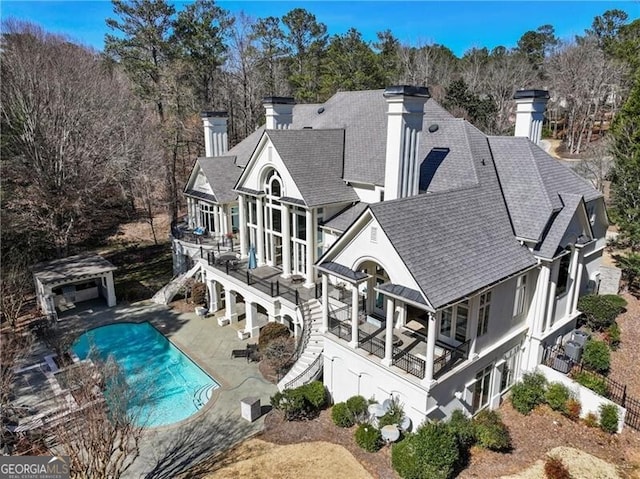 rear view of house with driveway, a shingled roof, a patio, a chimney, and stairway