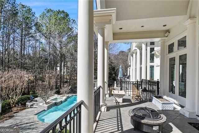 balcony with a fire pit, a patio area, and a pool with connected hot tub