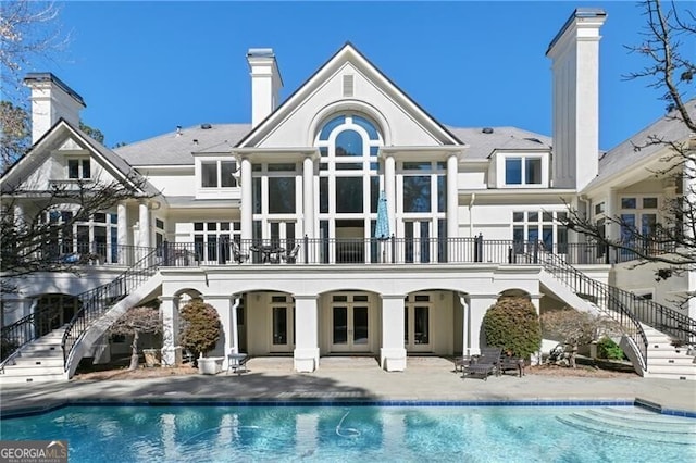 rear view of property featuring an outdoor pool, french doors, a patio, and stairs