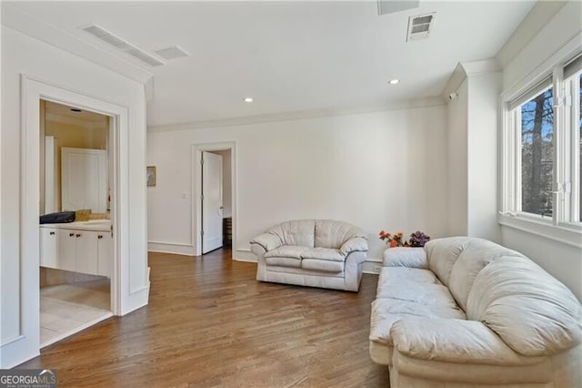 living area with wood finished floors, visible vents, and crown molding