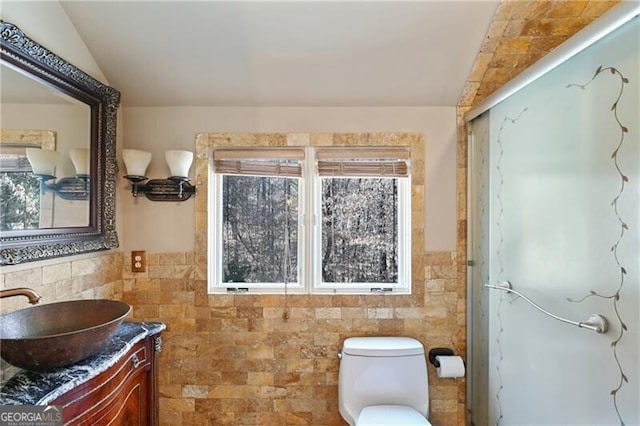 full bathroom featuring lofted ceiling, toilet, vanity, tile walls, and wainscoting