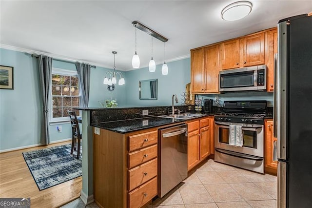 kitchen featuring stainless steel appliances, a peninsula, hanging light fixtures, brown cabinets, and dark stone countertops