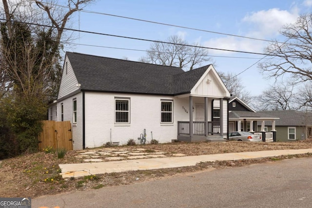 view of front of property featuring covered porch, brick siding, a shingled roof, and a gate