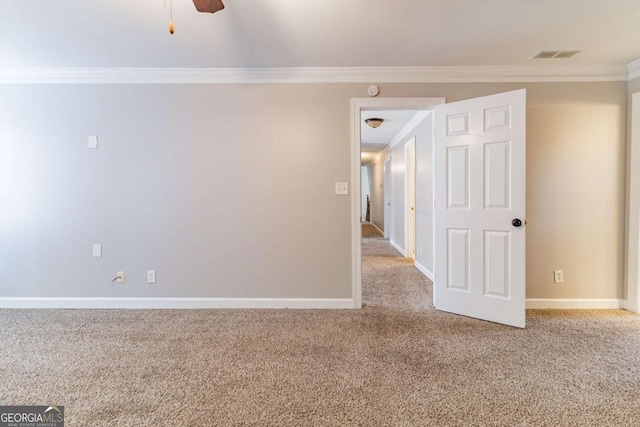 carpeted spare room with visible vents, crown molding, baseboards, and ceiling fan