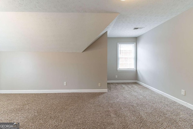 bonus room with baseboards, visible vents, vaulted ceiling, a textured ceiling, and carpet flooring