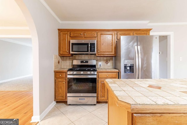 kitchen featuring arched walkways, stainless steel appliances, brown cabinetry, and decorative backsplash