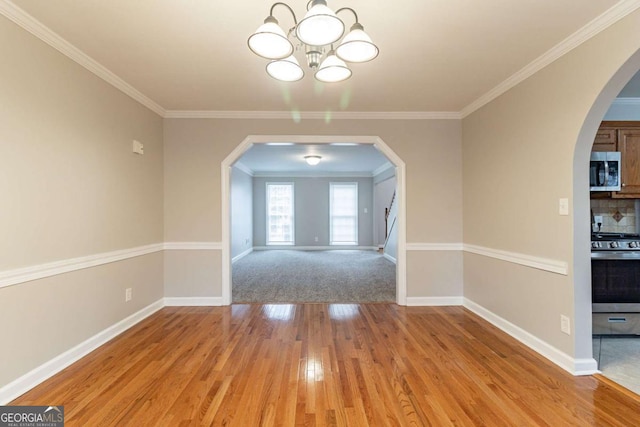 unfurnished dining area featuring ornamental molding, arched walkways, baseboards, and light wood finished floors