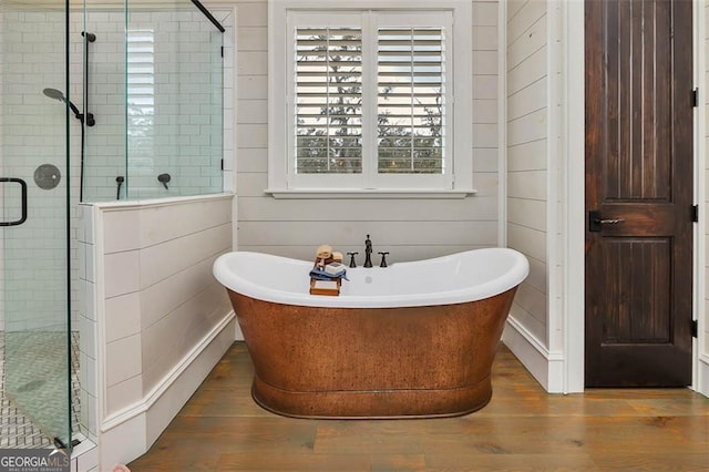 bathroom featuring a freestanding bath, wood finished floors, a shower stall, and wooden walls