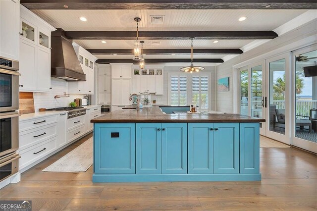 174 Bartram Way, Waverly, GA 31565 - kitchen featuring custom exhaust hood, a warming drawer, white cabinetry, tasteful backsplash, and an island with sink