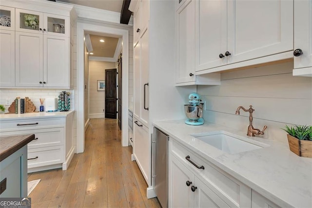 kitchen featuring light wood-style flooring, decorative backsplash, white cabinets, a sink, and light stone countertops