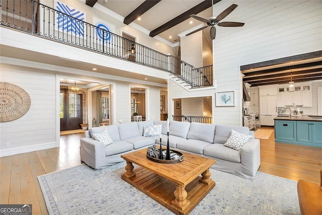 living area with stairs, beam ceiling, ceiling fan with notable chandelier, and hardwood / wood-style flooring