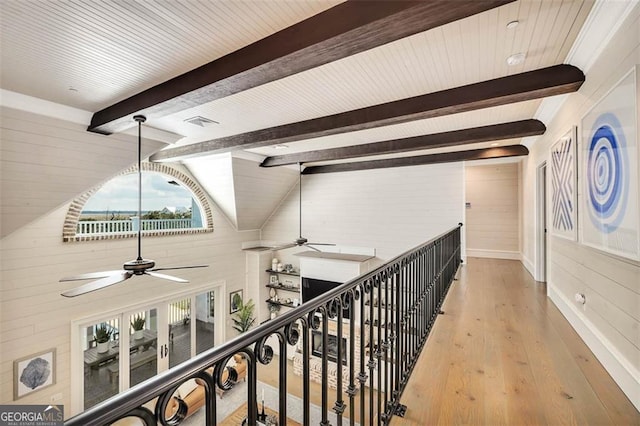 corridor with wood walls, lofted ceiling with beams, and wood finished floors