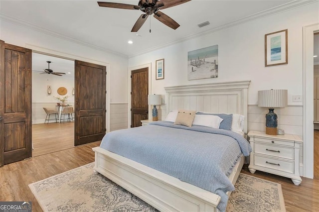 bedroom with a wainscoted wall, ornamental molding, wood finished floors, and visible vents