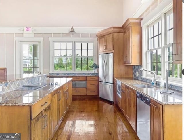 kitchen with appliances with stainless steel finishes, a healthy amount of sunlight, a sink, and light stone countertops