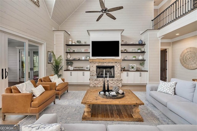 living room with a ceiling fan, ornate columns, wood walls, a brick fireplace, and high vaulted ceiling