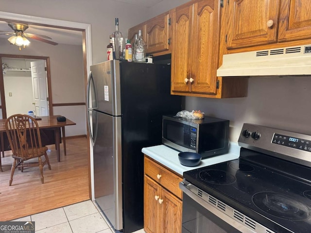 kitchen featuring light tile patterned flooring, under cabinet range hood, light countertops, appliances with stainless steel finishes, and brown cabinets