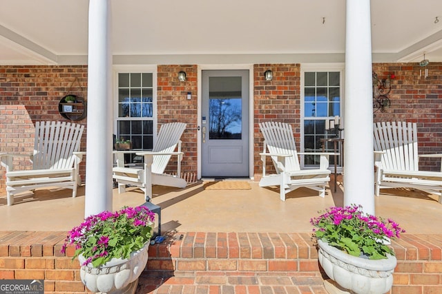 view of exterior entry featuring covered porch and brick siding