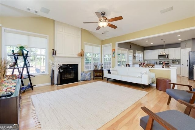 living room featuring a large fireplace, visible vents, vaulted ceiling, and light wood finished floors