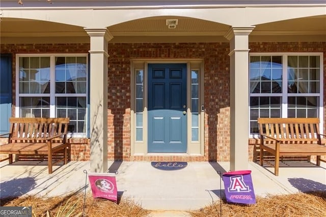 doorway to property with a porch and brick siding