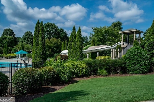 view of community featuring fence, a pool, and a lawn