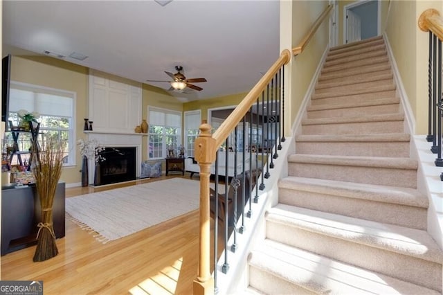 stairway featuring ceiling fan, a fireplace, baseboards, and wood finished floors