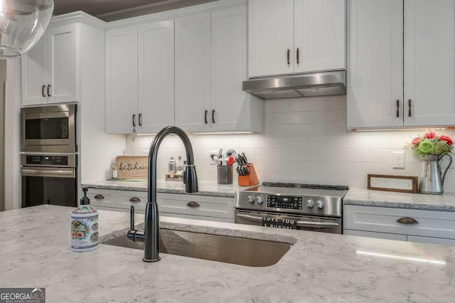 kitchen with under cabinet range hood, stainless steel appliances, a sink, white cabinetry, and decorative backsplash