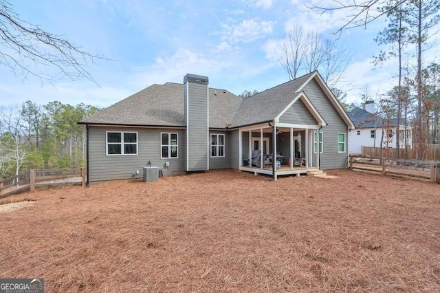 back of house with a fenced backyard, a chimney, a shingled roof, and central AC