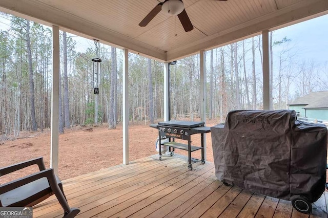 wooden terrace with ceiling fan, grilling area, and a view of trees